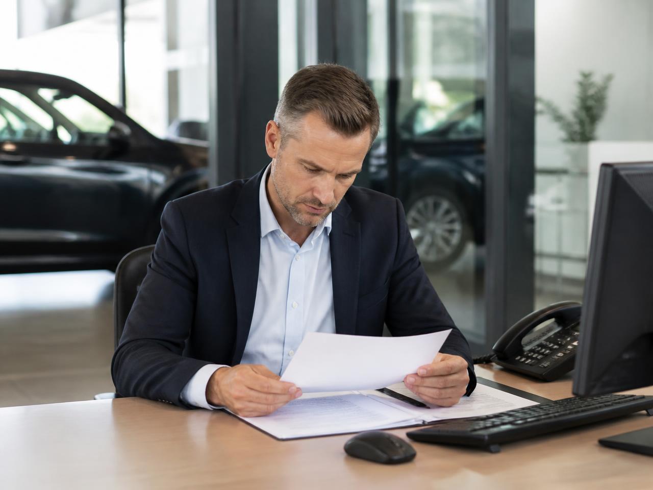 A dealership manager reviewing acquisition numbers at a desk